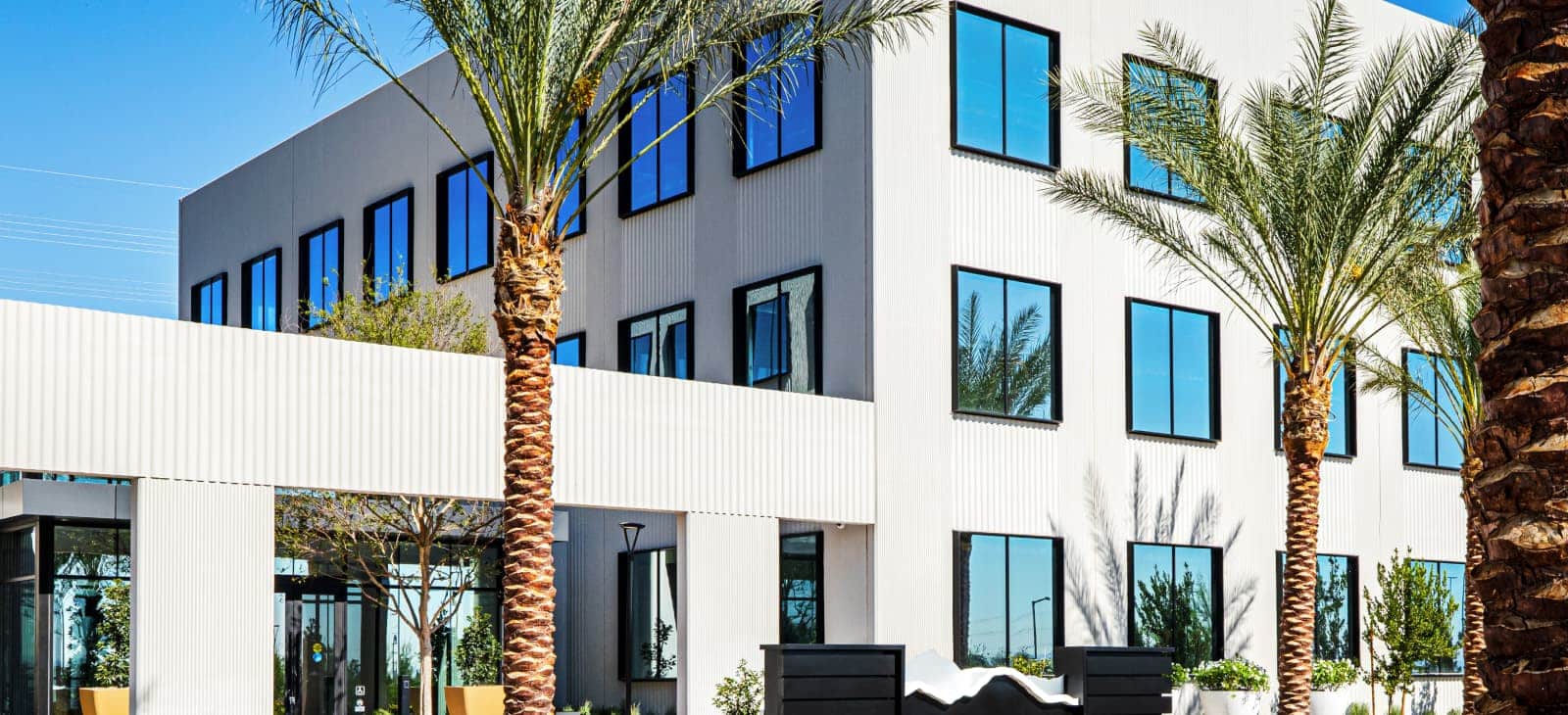 Modern Multi Story Building With Metal And White Facade And Palm Trees Hero
