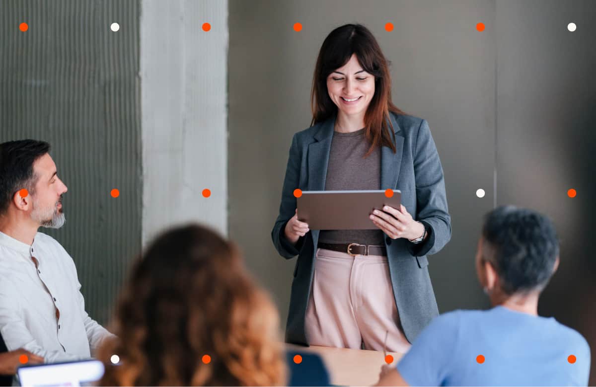 Woman Holding Tablet Presenting To Group In Modern Office