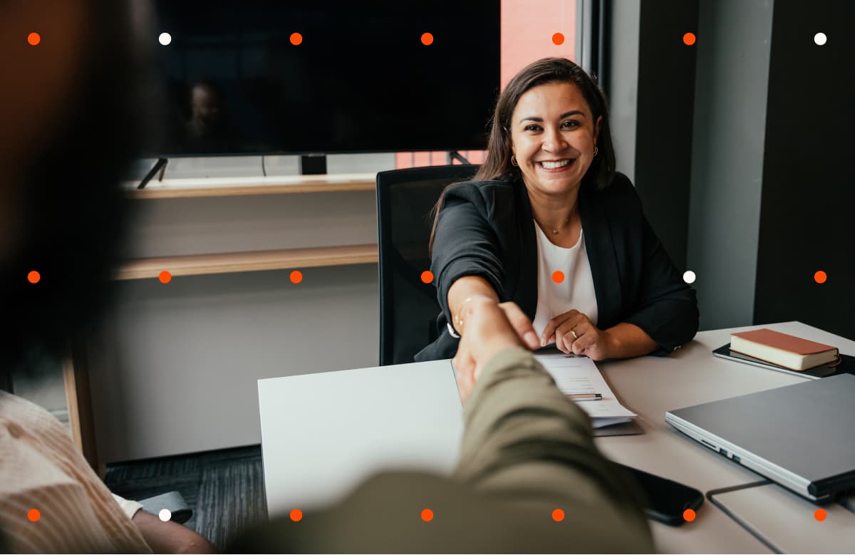 Woman Shaking Hands With Person Across Desk In Modern Office